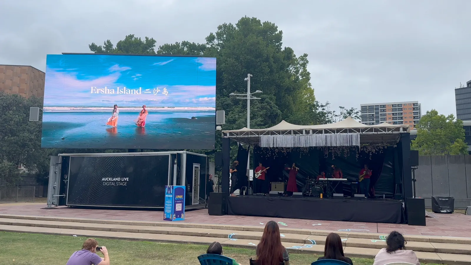 Edition 4 at Aotea Square: the Auckland Live Digital Stage with Ersha Island 二沙岛 performing, their name on the big screen, audience on the grass